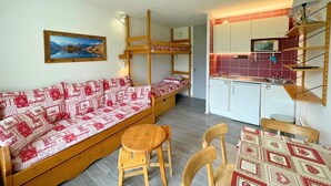 Une pièce de taille modeste comprenant un lit superposé, un canapé, une petite table à manger et un coin cuisine.