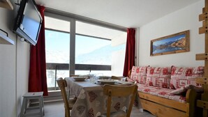 Une pièce chaleureuse avec une table à manger dressée pour deux personnes, un canapé, un téléviseur et une fenêtre donnant sur les montagnes.