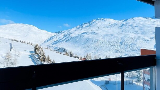 Une vue sur les montagnes depuis un balcon, avec des pentes enneigées et un ciel bleu dégagé.