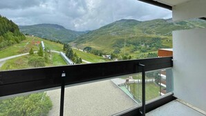 Un balcon donnant sur un paysage montagneux, une voie ferrée et un petit bâtiment.