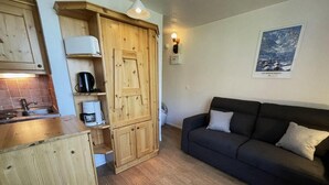 A compact living space with a kitchenette, wooden cabinets, a sofa, and a wall-mounted light fixture. - 10m from ski slopes, 6th floor, view resort, balcony, tv, 13m², Les Menuires (Les Menuires)