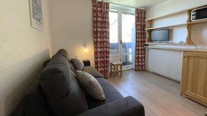 A cozy living room with a sofa, a small table, and a television on a wooden shelf. - 10m from ski slopes, 6th floor, view resort, balcony, tv, 13m², Les Menuires (Les Menuires)