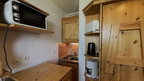 A compact kitchen with wooden cabinets, a microwave, a coffee maker, and a sink. - 10m from ski slopes, 6th floor, view resort, balcony, tv, 13m², Les Menuires (Les Menuires)