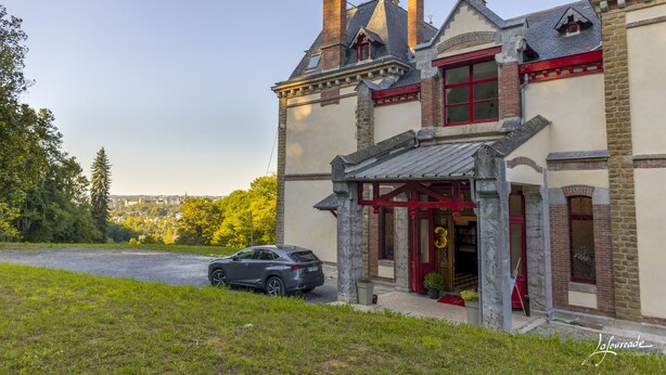 A historic building with a stone facade, red accents, and a parked car in front. - Château de La Tisnère on the outskirts of Pau (Gelos)