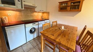 A compact kitchen with a microwave, washing machine, and a wooden dining table with chairs. - 1st floor, view ski slopes, balcony, ski locker, 33m², Saint Martin de Belleville (Saint-Martin-de-Belleville)