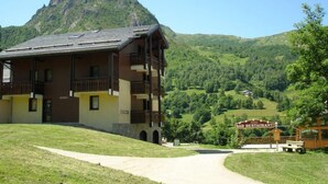 A mountain lodge with a balcony, a path leading to the entrance, and a view of the surrounding green hills. - 1st floor, view ski slopes, balcony, ski locker, 33m², Saint Martin de Belleville (Saint-Martin-de-Belleville)