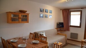A cozy room with a wooden dining table set for four, a sofa, a television on a stand, and a window with curtains. - 1st floor, view ski slopes, balcony, ski locker, 33m², Saint Martin de Belleville (Saint-Martin-de-Belleville)