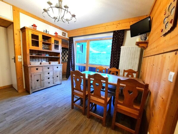 A wooden interior with a dining table and chairs, a kitchen with cabinets, and a TV mounted on the wall. - 10m from ski slopes, 1st floor, view mountain, balcony, tv, ski locker, 32m², Les Menuires (Les Menuires)