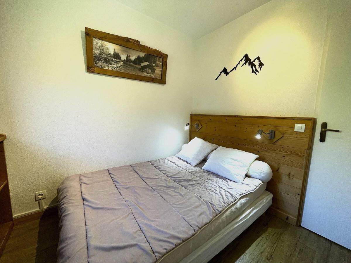 A single bed with a wooden headboard and a headlamp, a framed picture on the wall, and a mountain silhouette decoration.