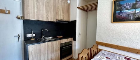 A compact kitchen with wooden cabinets, a black countertop, and a built-in oven.
