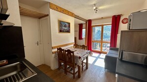 A kitchen with a dining area, a large window with red curtains, and a view of the outdoors.