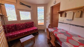 Una habitación acogedora con un sofá rojo, una mesa de comedor de madera y una ventana con vistas a zonas verdes.