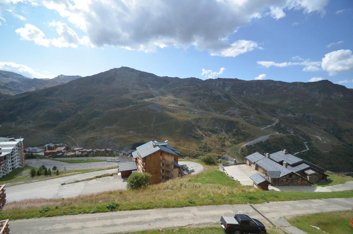 A mountainous landscape with traditional wooden buildings, a parking area, and a clear sky.