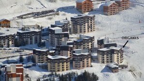 A snow-covered ski resort with multiple high-rise buildings, including a hotel marked as "ORIGANES." - 300m from resort center, 2nd floor, balcony, tv, 67m², Les Menuires (Les Menuires)