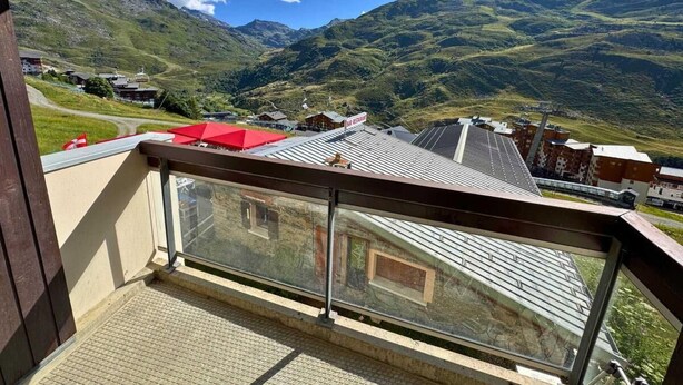 A balcony with a view of a mountainous landscape, a red umbrella, and a building with a sign. - 300m from resort center, 2nd floor, balcony, tv, 67m², Les Menuires (Les Menuires)