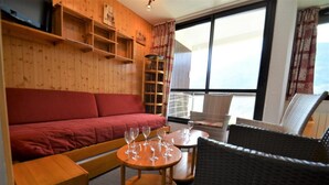 A cozy room with a red sofa, wicker chairs, a wooden table with wine glasses, and a large window with curtains. - 300m from resort center, 2nd floor, balcony, tv, 67m², Les Menuires (Les Menuires)