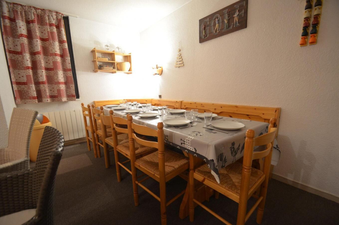 A dining room with a long wooden table set for four, surrounded by wooden chairs.