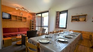 A dining area with a long table set for four, wooden furniture, and a television on the wall. - 300m from resort center, 2nd floor, balcony, tv, 67m², Les Menuires (Les Menuires)