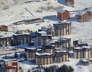 A snow-covered ski resort with multiple high-rise buildings, including a hotel marked as "ORIGANES."