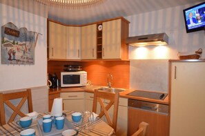 A compact kitchen with a microwave, sink, and wooden cabinets. There is a table with blue cups and a pitcher. - 50m from shops, 5th floor, tv, ski locker, 26m², Les Menuires (Les Menuires)