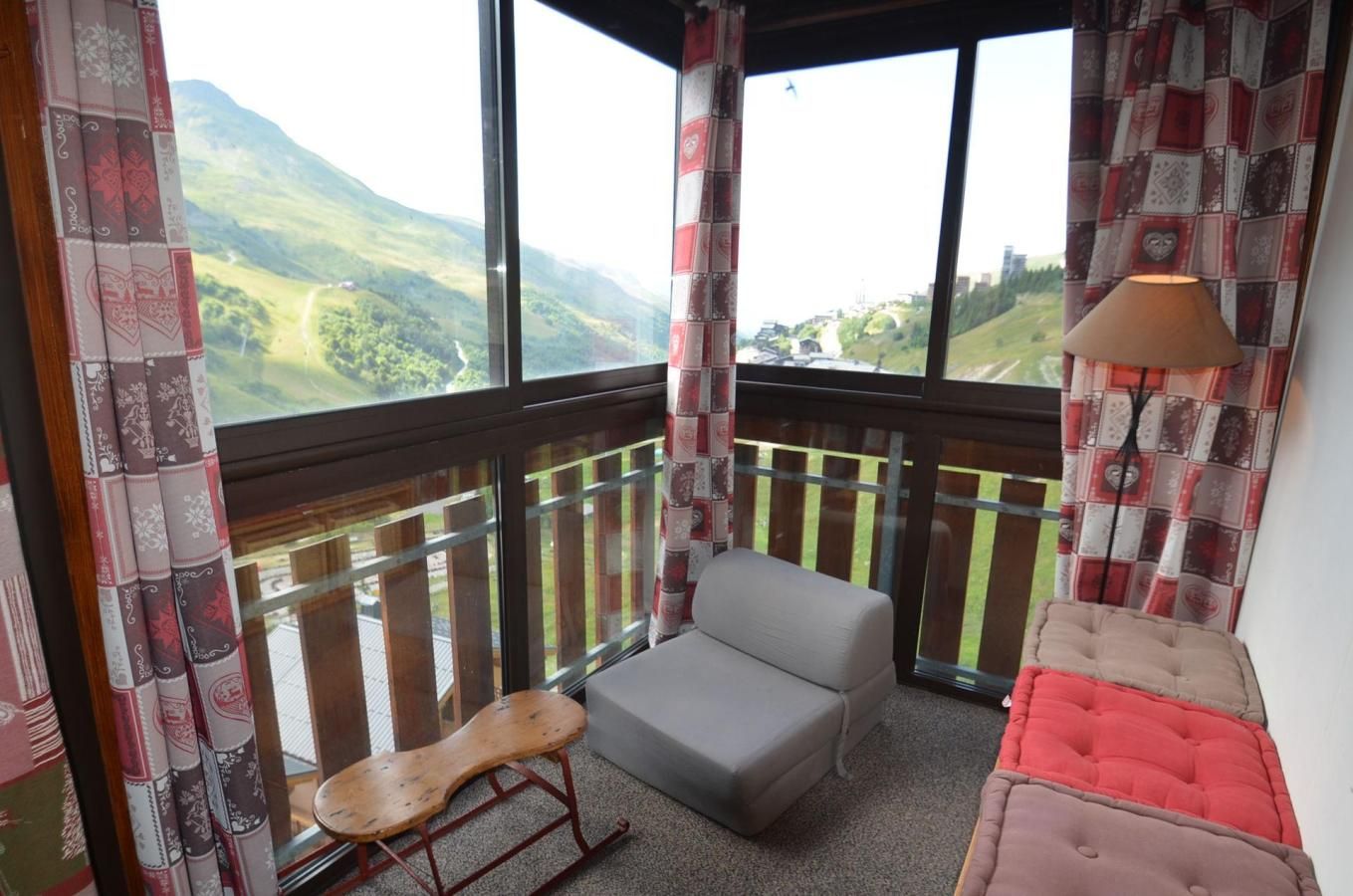 Ein Balkon mit gepolsterten Sitzgelegenheiten, einem kleinen Holztisch und Blick auf eine grüne Landschaft.