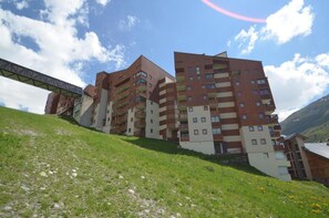 Un immeuble à plusieurs étages doté de balcons, d’un pont piétonnier et situé dans un paysage vallonné.