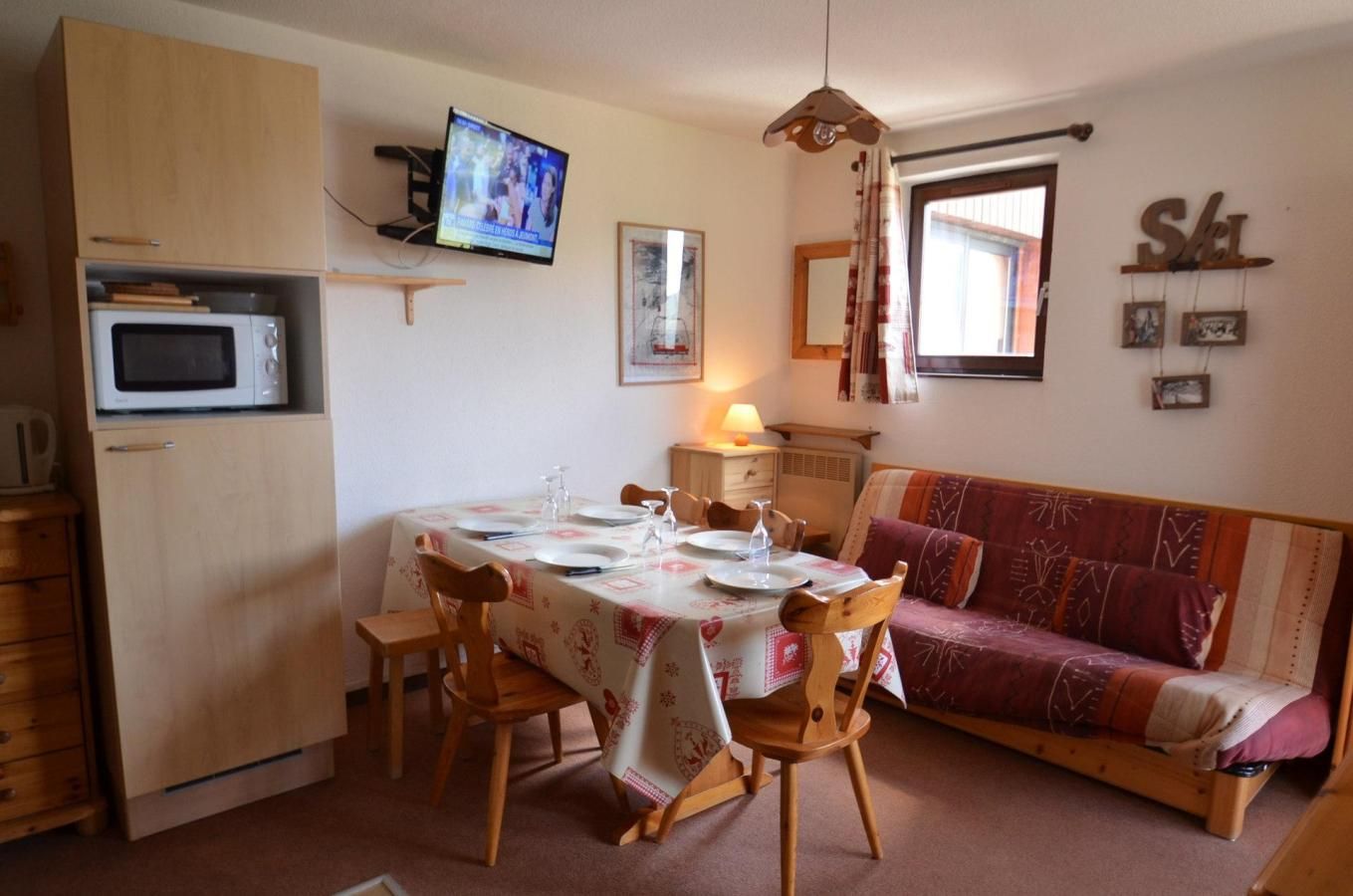 Un espacio habitable compacto con una mesa de comedor para cuatro personas, un sofá, un televisor y un microondas.