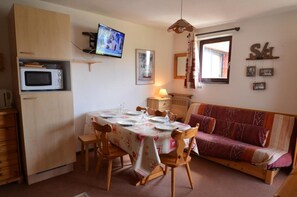 A compact living space with a dining table set for four, a sofa, a television, and a microwave. - 10m from ski slopes, 6th floor, tv, ski locker, 28m², Les Menuires (Les Menuires)