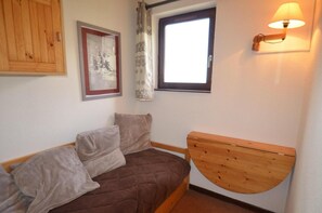 A bedroom with a bed, pillows, a window, a curtain, a wall-mounted lamp, and a wooden cabinet. - 10m from ski slopes, 6th floor, tv, ski locker, 28m², Les Menuires (Les Menuires)