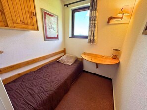 A small, cozy room with a single bed, a wooden shelf with a lamp, a window with curtains, and a framed picture on the wall. - 10m from ski slopes, 6th floor, tv, ski locker, 28m², Les Menuires (Les Menuires)