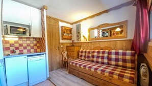 Una habitación compacta con kitchenette, una cama con manta escocesa y un cabecero de madera.