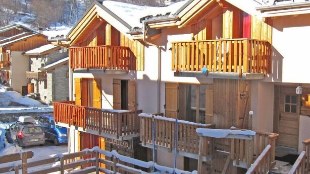 Une rangée de chalets en bois dotés de balcons, chacun ayant une porte en bois et des volets aux fenêtres, le tout situé dans un paysage enneigé.