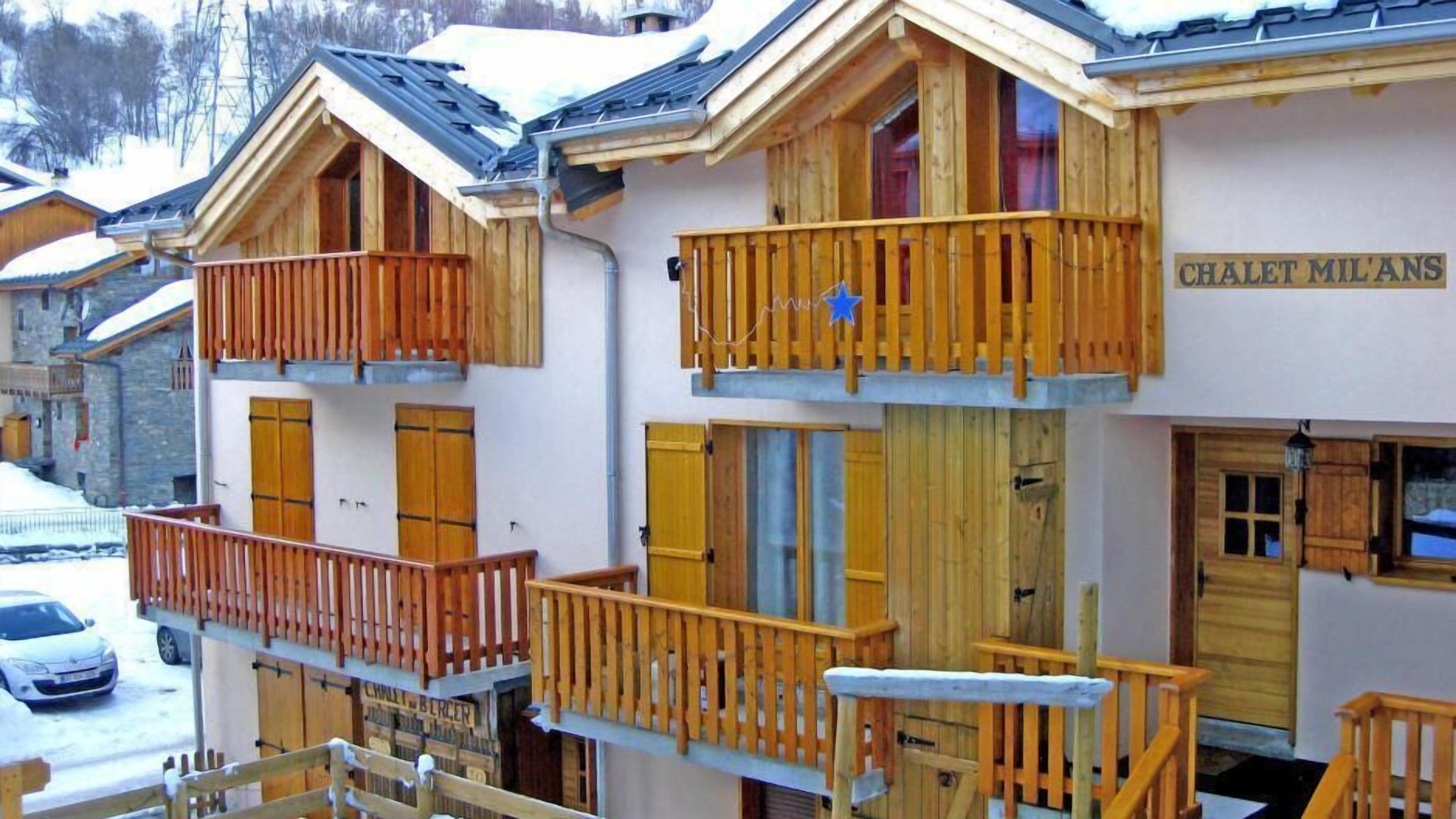 A chalet with wooden balconies and a sign reading "CHALET MIL'ANS".