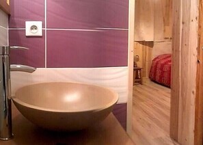 Un baño con un lavamanos grande y redondo, un espejo y una pared de azulejos morados.