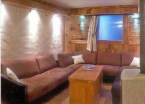 Una habitación acogedora con detalles de madera, un sofá marrón, una mesa de centro de madera y una ventana con cortinas.