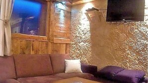 Un salon chaleureux avec un mur en bois, un téléviseur à écran plat fixé au-dessus d’une cheminée et un canapé confortable.