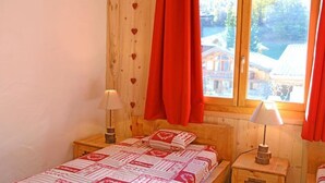 A cozy room with a bed, two bedside lamps, and a window with red curtains. - Chalet, sauna, balcony, fireplace or stove, parking, tv, ski locker, 140m², Les Menuires (Saint-Martin-de-Belleville)