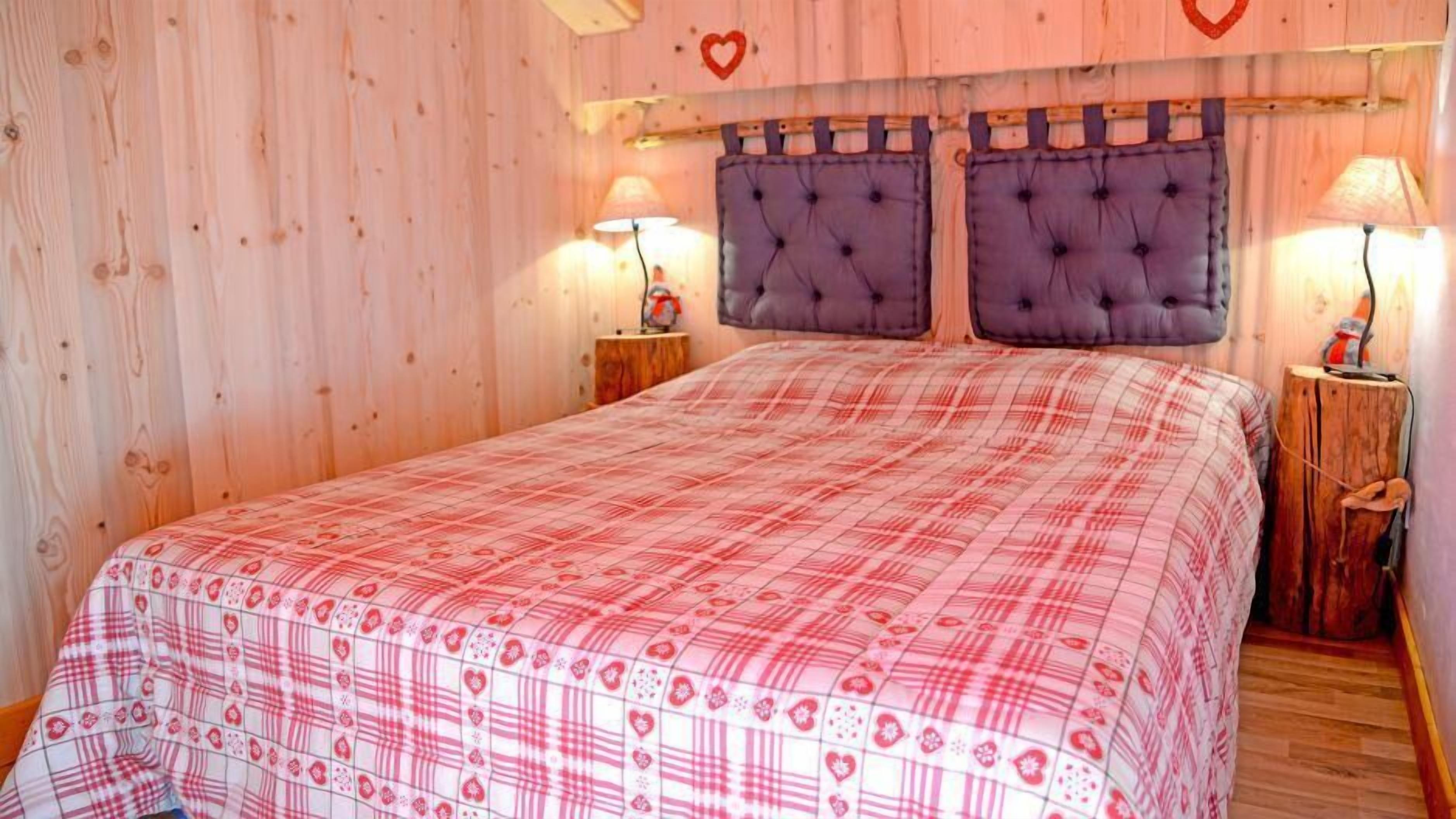 Una camera da letto con copripiumino a quadri, pareti in legno e due comodini con lampade.