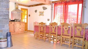 A dining area with a wooden table and chairs, a kitchen with a stove, and stone walls. - Chalet, sauna, balcony, fireplace or stove, parking, tv, ski locker, 140m², Les Menuires (Saint-Martin-de-Belleville)
