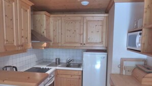 A compact kitchen with wooden cabinets, a white refrigerator, a stove, and a sink. - 2nd floor, terrace, tv, ski locker, 71m², Méribel (Méribel - Les Allues)