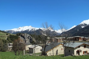 A mountain village with traditional buildings, a clear sky, and snow-capped peaks in the background.
