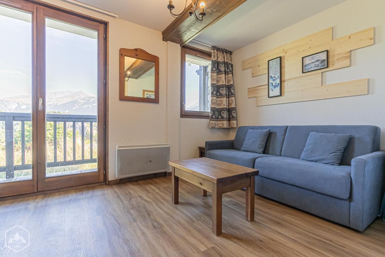 A living room with a sofa, a wooden table, a radiator, a mirror, and a window with a view of mountains.