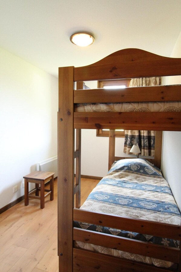 Una cama litera con un colchón estampado, un taburete de madera pequeño y una lámpara en el techo.