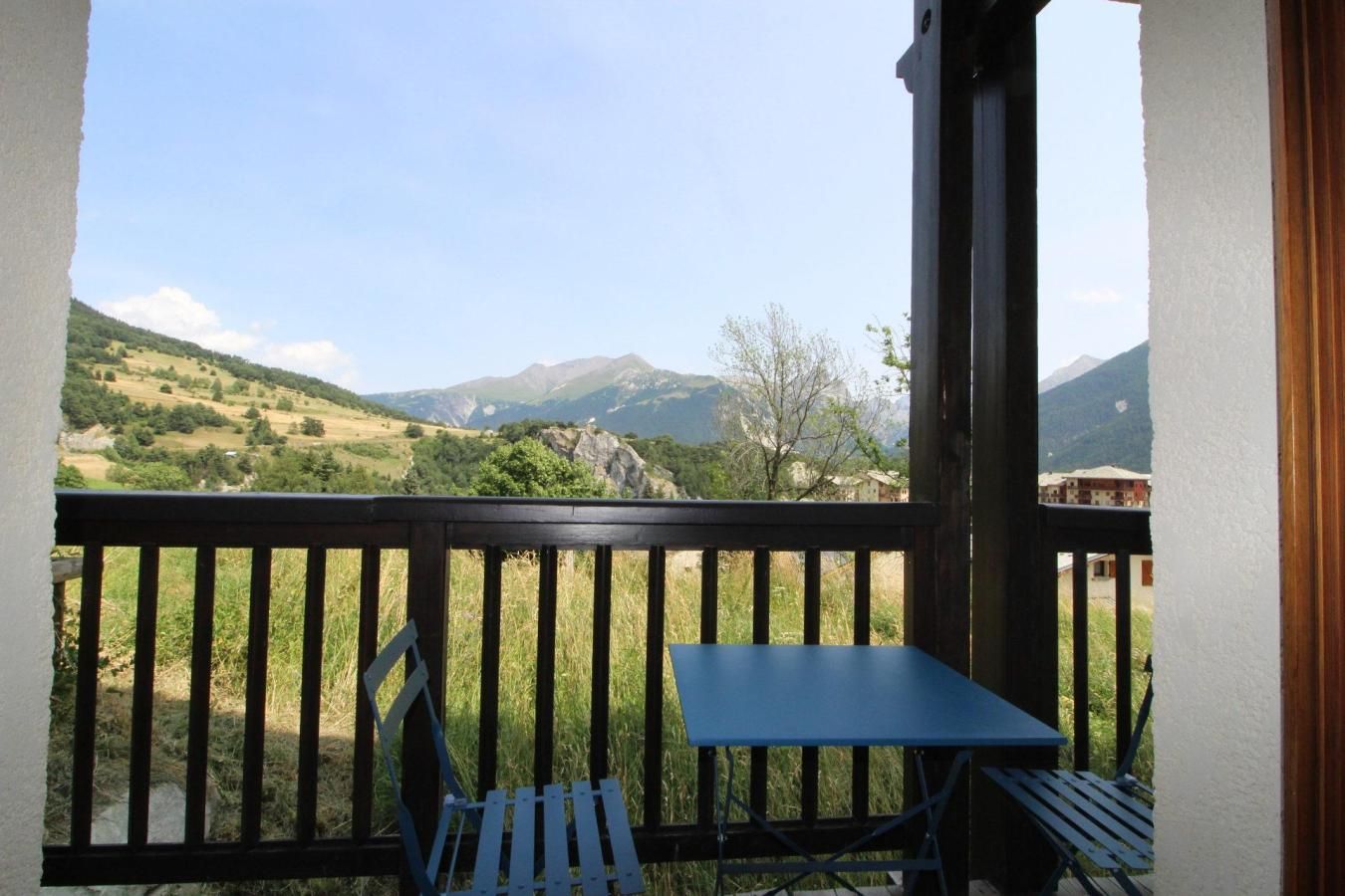 A balcony with a table and chairs, overlooking a mountainous landscape.