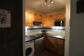A compact kitchen with wooden cabinets, a dishwasher, a washing machine, and a microwave.