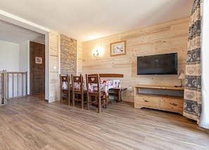 A wooden interior with a dining area, a TV, and a stone wall.