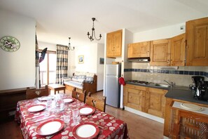 A compact kitchen with wooden cabinets, a dining table set with red tablecloths, and a refrigerator.