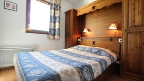 Une chambre à coucher avec une tête de lit en bois, une couvre-lit à motifs, une fenêtre avec des rideaux et une lampe fixée au mur.