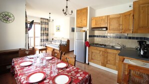 Une cuisine compacte avec des meubles en bois, un four encastré et un coin repas agrémenté d’une nappe rouge et d’assiettes.