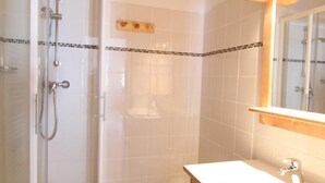 Une salle de bain avec une douche à parois de verre, des toilettes blanches et un meuble-lavabo en bois avec un miroir.